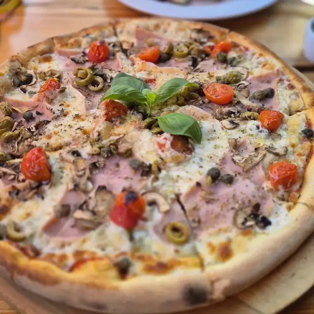 Pizza z szynką, pieczarkami, oliwkami i pomidorkami na drewnianej desce